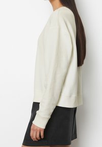 Sudadera de un tono beige claro con cuello redondo, puños y dobladillo acanalados; combinada con una falda ajustada oscura; textura suave, diseño casual.