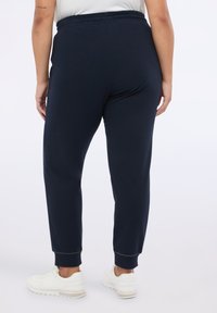 Granatowe spodnie dresowe z elastycznym paskiem w talii i dopasowanymi mankietami. Wykonane z miękkiego materiału, charakteryzują się prostym wzorem bez widocznych dekoracji.