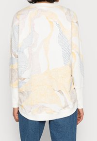 Top ligero de manga larga con un fondo blanco, que presenta patrones abstractos en suaves tonos pastel de amarillo, rosa y azul. Puños acanalados.