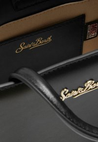 Sac �à main en cuir noir arborant un logo doré "Saint Barth", texture lisse et intérieur en tissu beige avec des détails matériels minimaux.