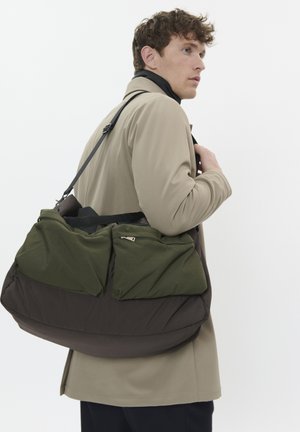 Sacoche épaule marron foncé et verte de forme arrondie, avec deux poches zippées à l'avant et un design rembourré. Bandoulière détachable incluse.