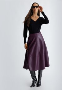 Top negro de manga larga con escote en V, combinado con una falda de cuero morada a media longitud con cintura alta y hebillas laterales. Botas negras brillantes hasta la rodilla.