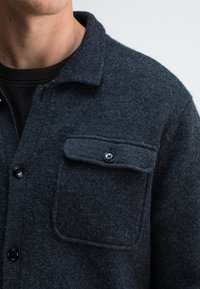 Dunkelgraues Wollflanellhemd mit einer Knopftasche auf der Brust, einem klassischen Kragen und strukturiertem Stoff für Wärme und Komfort.