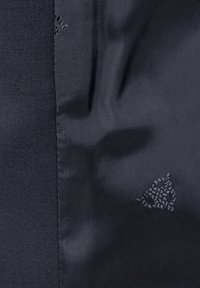 Schwarzer Stoff mit einem strukturierten Muster auf einer Seite, im Kontrast zu glattem Material. Zeigt strukturierte Formen und gestickte Details.