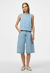 Ljusblå denimoutfit bestående av en ärmlös topp och vida shorts, båda med subtila dekorationer, kompletterad med ljusa skor.