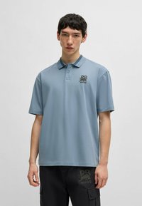 Paita polo dalam kain biru muda, dilengkapi dengan kerah, placket dua tombol, dan logo hitam di dada. Lengan pendek dengan potongan yang nyaman.