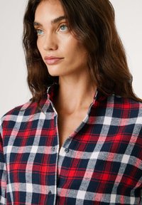Rood, marineblauw en witte geblokte flanellen shirt met een kraag, knoopsluiting en een zachte textuur, weergegeven op het bovenlichaam van een model.