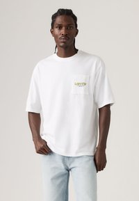 Λευκό T-shirt με κοντά μανίκια και τσέπη στο στήθος που φέρει κίτρινο λογότυπο "Levi's". Κατασκευασμένο από βαμβάκι, με άνετη εφαρμογή και απαλό ύφασμα.