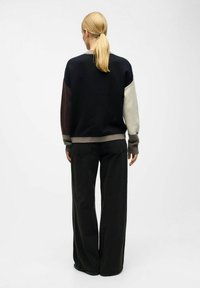 Strikket sweater med multifarvede ærmer (sort, grå, brun) og ribbet kant. Matchet med brede sorte jeans. Glat tekstur.