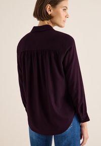 Langærmet, mørkebl�å bluse med krave, plisseret ryg og knaplukninger ved håndleddene. Blødt materiale, parret med blå denim.
