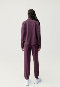 Mörkröd idrottsdräkt med lång ärm och elastiska ärmslut, med hög krage och smalnande joggers. Vita sneakers fulländar looken.