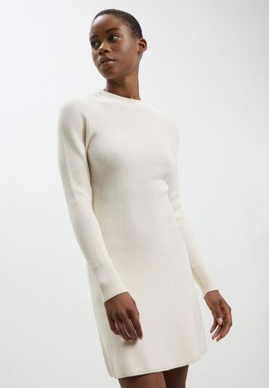 Robe en tricot côtelé de couleur crème, présentant des manches longues, un col montant et une silhouette ajustée qui s'effile au niveau de l'ourlet.