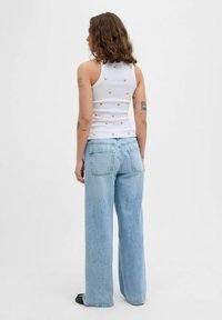 Valge spordisärk, millel on oranž südameprindid, koos helesiniste laia säärega teksadega. Puuvillane materjal, lõdva istuvuse ja nähtavate tagataskutega.