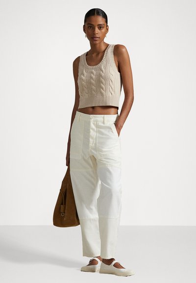 Beige pletený krátký top, bílé široké kalhoty s vysokým pasem a béžové nazouvací boty. Modelka nese hnědou semišovou tašku.