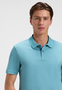 Kortærmet polo-shirt i lys blå med teksturmønster, med krave og enkelt knaplukning.