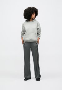 Hall halliga kapuutsiga pusa esitasku ja valge logoga, kombineeritud hallide dressipükstega, millel on valged triibud ja logo, kantud mustade jalanõudega.