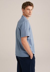 Camisa de manga corta azul claro hecha de suave algodón con un ajuste relajado y un cuello clásico. Presenta un dobladillo recto y detalles de costura mínimos.