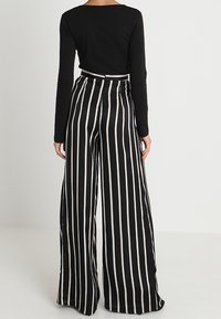 Haut noir à manches longues associé à un pantalon taille haute à jambe large avec des rayures verticales noires et beiges, texture de tissu lisse.