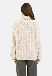 Fellstrickpullover in Creme, mit hohem Kragen, weiten Ärmeln und einem strukturierten Muster. Weicher, strukturierter Stoff bietet Wärme.