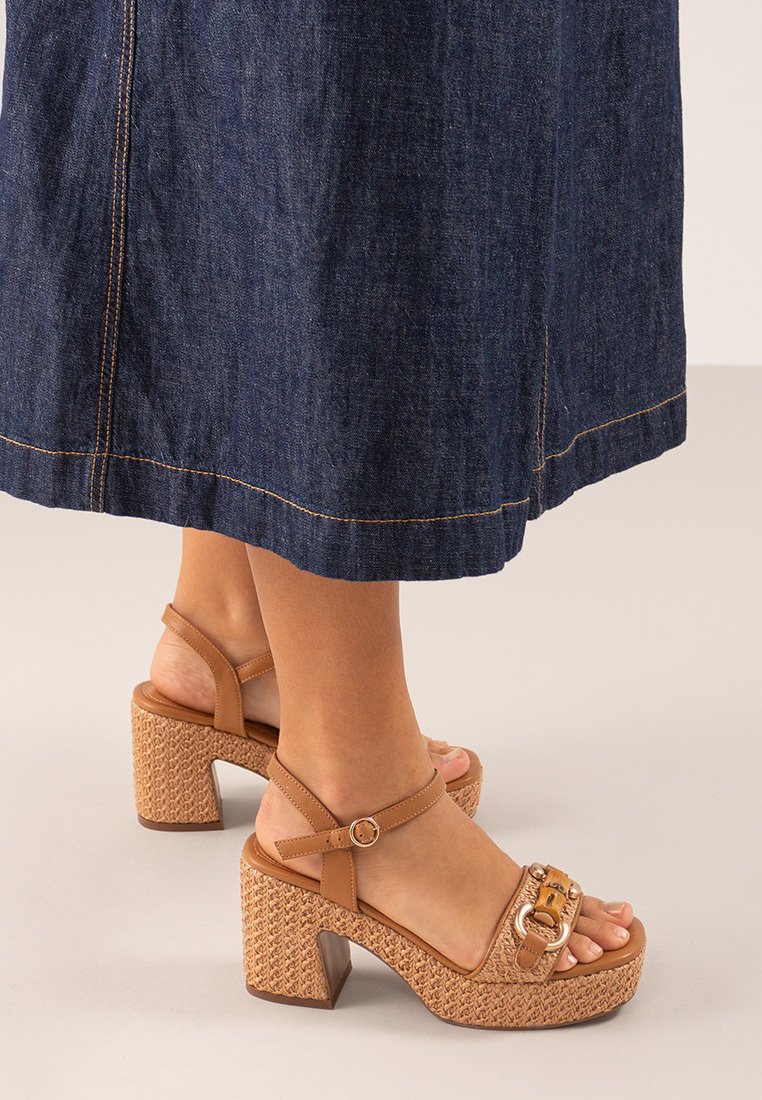 Sandalias de plataforma marrones con punta abierta, correa ajustable y una suela texturizada de estilo tejido. Presentan una herrajes decorativos en la parte superior.