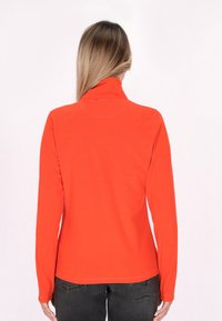 Langarm, hoge hals pullover van feloranje stof. Beschikt over een gladde textuur en een getailleerde pasvorm, gecombineerd met donkere jeans.