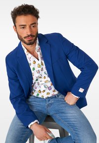 Mėlynas švarkas virš balto marškinėlio su spalvingais animacinių filmų motyvais, derinamas su šviesiai mėlynomis džinsinėmis kelnėmis. Ant rankovės yra logotipo pleistras.