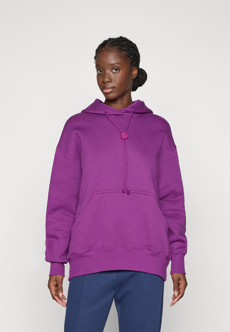 Lila Kapuzenpullover mit Kordelzug, Fronttasche und gerippten Bündchen; aus einem weichen, strukturierten Stoff; kombiniert mit dunkelblauen Hosen.