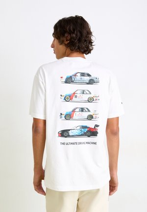 White cotton t-shirt featuring a printed graphic of four stylized racing cars in varying colors, with text below stating "THE ULTIMATE DRIVING MACHINE."