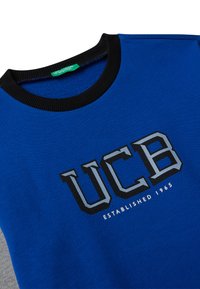Felpa azzurra con colletto a girocollo nero. Presenta il logo "UCB" in grigio e bianco, con il testo "Established 1965" sottostante. Tessuto morbido.
