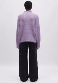 Lavendelfarbenes Strickpullover mit hohem Kragen, gerippter Struktur und einem leicht lässigen Schnitt, kombiniert mit schwarzen weit geschnittenen Hosen.