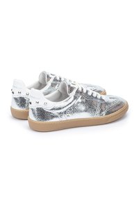 Zapatillas metálicas plateadas con una superficie texturizada, cordones blancos, suela de goma marrón y tachuelas decorativas en el talón.