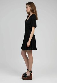 Robe noire à manches courtes, avec un décolleté en V profond et une taille froncée. Portée avec des sandales à plateforme noires dotées de semelles en bois et de clous en or.