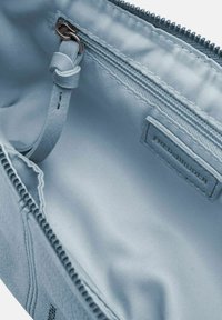 Interno di una borsa di pelle azzurro chiaro con una tasca con cerniera e texture liscia. Presenta un'etichetta con marchio e bordi cuciti.