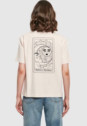 Helles beige T-Shirt aus Baumwolle mit einem schwarzen Linienstil-Design von Sonne und Mond mit Herzen, umrahmt von Wolken und dem Text "Sonnenliebhaber & Sternjäger."