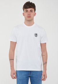 T-shirt bianco in cotone con collo rotondo, maniche corte e un piccolo logo nero sul petto sinistro. Tessuto morbido con una vestibilità classica.