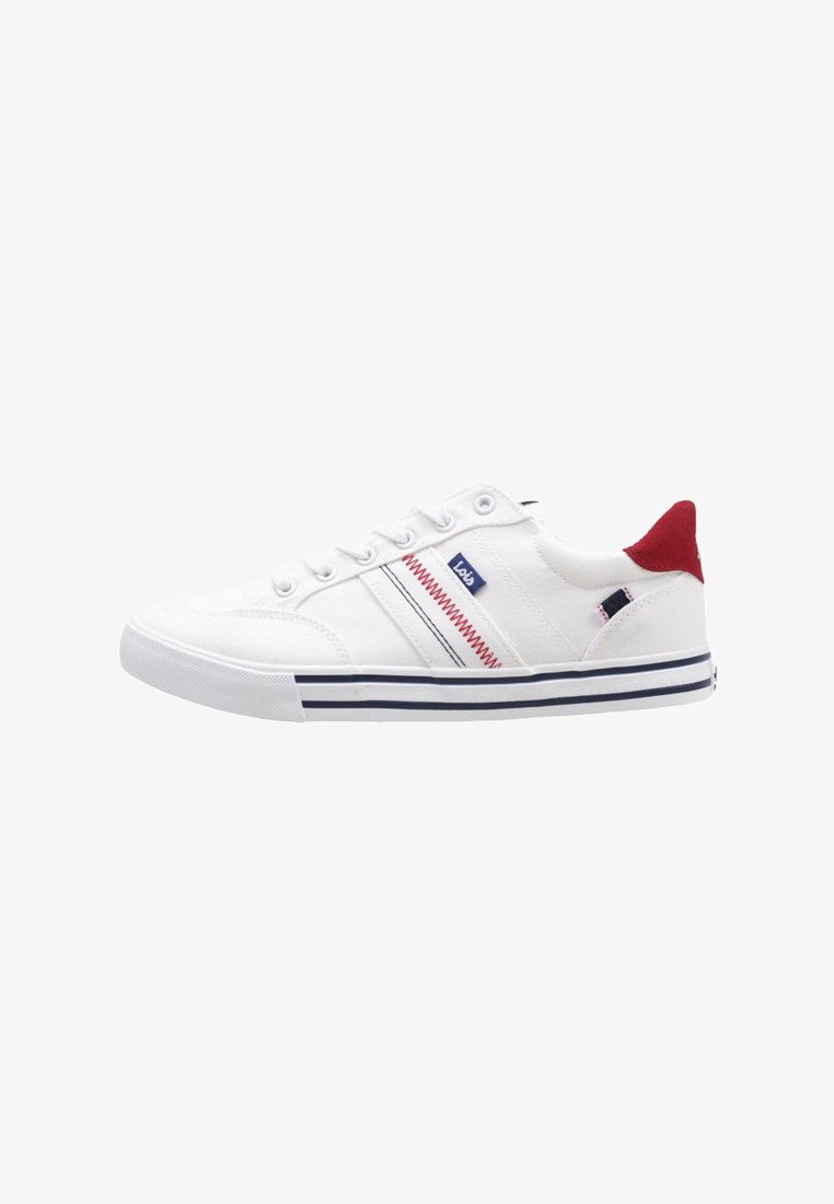 Zapatilla baja blanca con lengüeta trasera roja, costura en zigzag azul y roja en el costado, cordones blancos y suela a rayas azules.