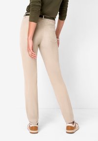 Beige bomullsblandade byxor med rak passform, bakfickor och minimala detaljer, tillsammans med ljusbruna sneakers.