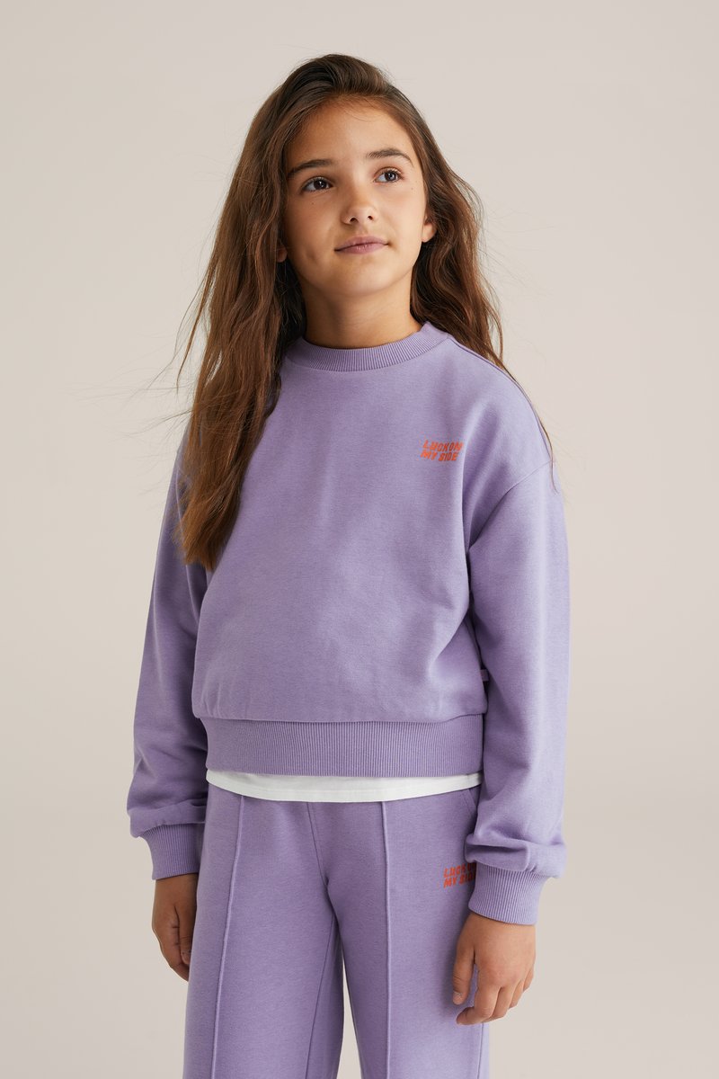 Lila Baumwoll-Sweatshirt mit Rundhalsausschnitt und gerippten Bündchen, mit dem Aufdruck "LUCKY ON MY SIDE" in kontrastierendem roten Stickerei.