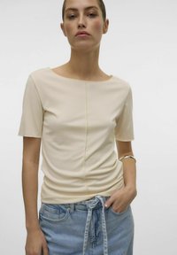 Beige t-shirts med korte ærmer og rund hals, med en central syning og blød tekstur, parret med lyseblå denim jeans.