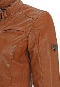 Braune Lederjacke mit Stehkragen, Reißverschluss-Brusttasche und einem Patch-Logo auf der Schulter. Glatte Textur und taillierte Passform.