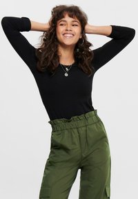 Schwarzes Langarmshirt kombiniert mit lockeren, hoch taillierten olivgrünen Hosen, die einen elastischen Bund und seitliche Taschen haben.