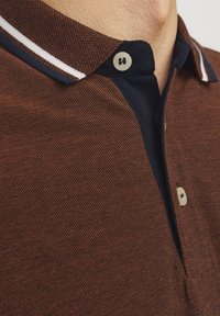 Roodachtige polo shirt met een gestructureerde stof, marineblauwe kraag, witte accentstrepen en twee knopen nabij de hals.