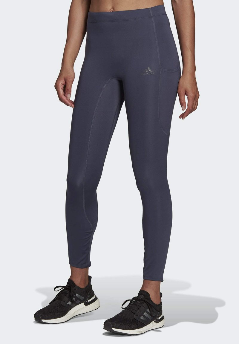Donkergrijze sportleggings van rekbaarheid, met een hoge tailleband en een zijzak, gecombineerd met zwarte hardloopschoenen.