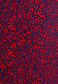 Tissu marine avec des points rouges éparpillés et irréguliers créant une surface texturée et motifée. Le design est audacieux et vibrant.