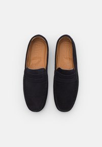 Mornarsko modri semiš loafers s gladko teksturo, oblikovani za enostavno obuvanje, s kontrastnim šivom in embosiranim logotipom na notranji strani.