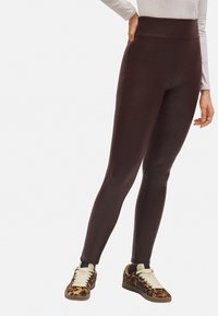 Leggings marrones de cintura alta hechos de una tela suave, con un ajuste ceñido y sin costuras visibles, combinados con zapatillas de estampado de leopardo.