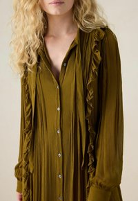 Robe longue verte olive en tissu texturé, avec des volants à l'avant et aux manches, et un design à boutons.