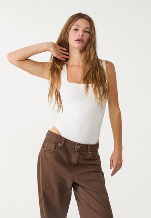 Biele body s obdĺžnikovým výstrihom kombinované s hnedými rifľovými nohavicami s vysokým pásom. Má hladkú textúru a priliehavý strih.