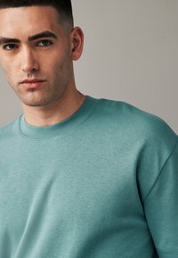 Helles Teal-Sweatshirt mit Rundhalsausschnitt und weicher Textur, mit minimalen Nähdetails und lockerer Passform.