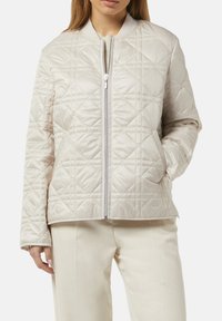 Beige gesteppte Jacke mit hohem Kragen, Frontreißverschluss und leichtem Finish. Mit Rautenmuster und Seitentaschen.